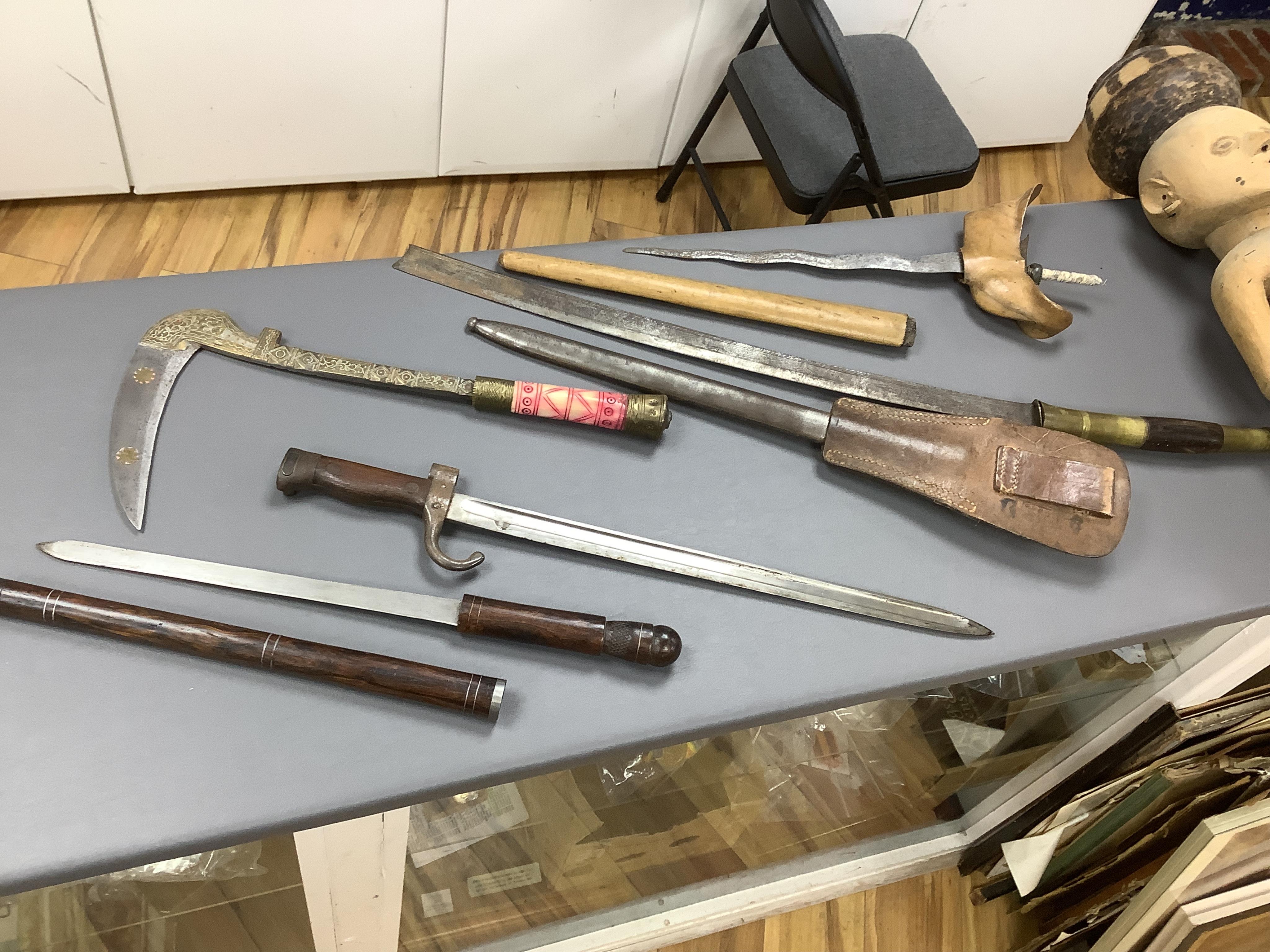 Eighteen assorted world weapons comprising a silver jambya (pommel missing), a knobkerry, a dha, two kris (one with handle missing), a lohar, three kukris, a djambok, a Chinese trousse, a chora, a flyssa, five others and